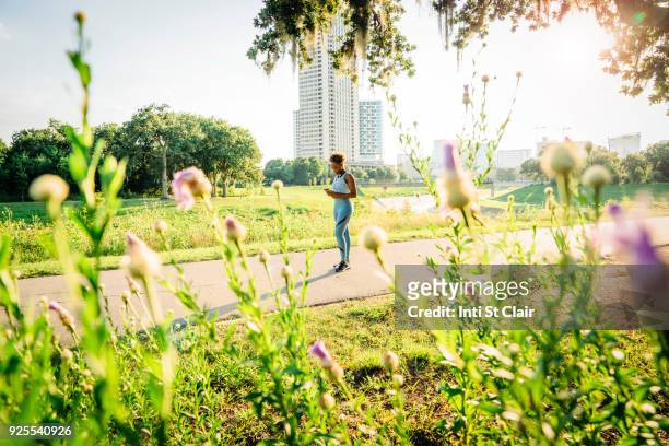 mixed race woman standing on running path in park beyond wildflowers - will houston fotografías e imágenes de stock