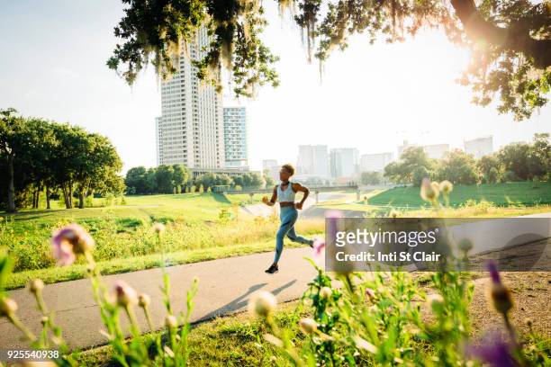 mixed race woman running on path in park beyond wildflowers - multiple smart devices stock-fotos und bilder