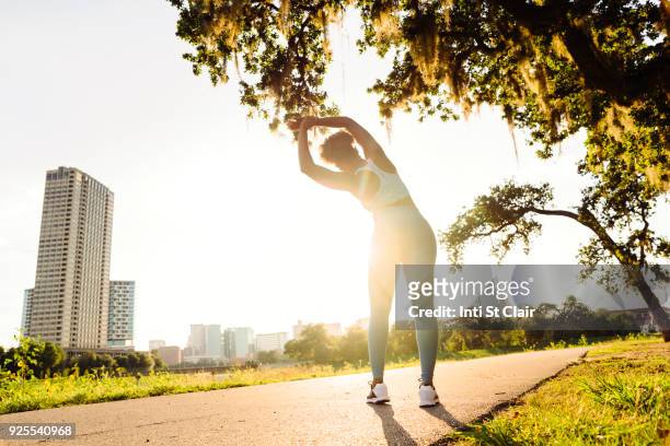 mixed race woman stretching on running path in park - woman stretching sunset stock-fotos und bilder
