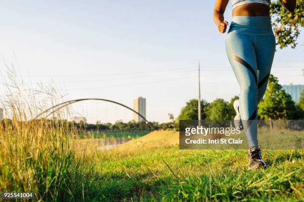 legs of mixed race woman running in grass near waterfront - will houston fotografías e imágenes de stock