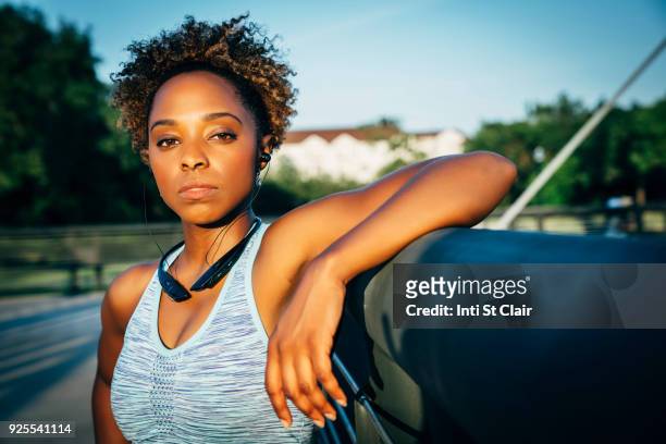 serious mixed race woman listening to earbuds on bridge - will houston fotografías e imágenes de stock