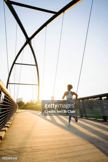 distant mixed race woman running on bridge - will houston fotografías e imágenes de stock