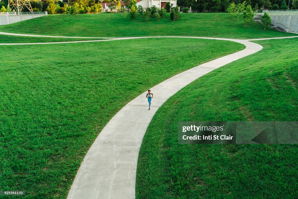 Distant mixed race woman running on winding path in park
