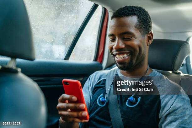 smiling black man texting on cell phone in car - black car photos et images de collection