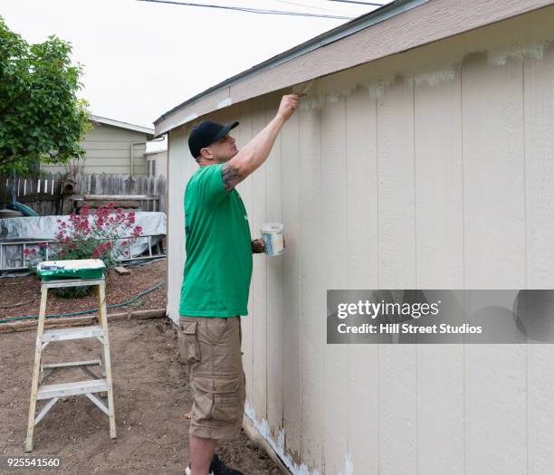 volunteering man painting siding on house - tool shed wall spaces stockfoto's en -beelden