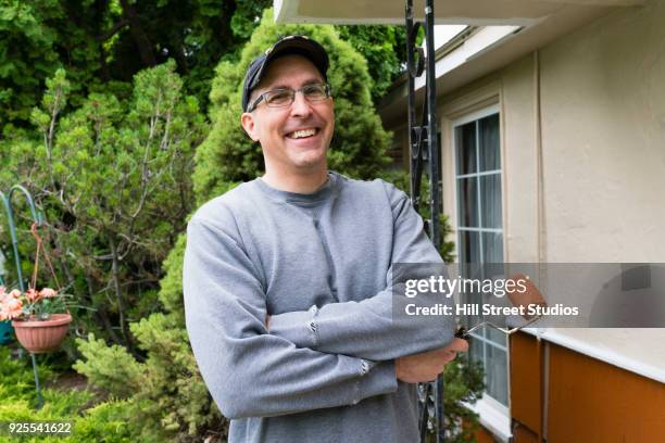 portrait of smiling man holding paint roller near house - welfare reform stock pictures, royalty-free photos & images