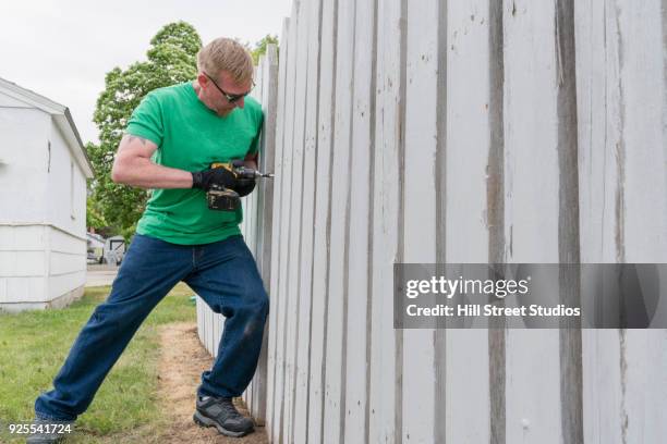 volunteering man repairing wooden fence with drill - fence stock pictures, royalty-free photos & images