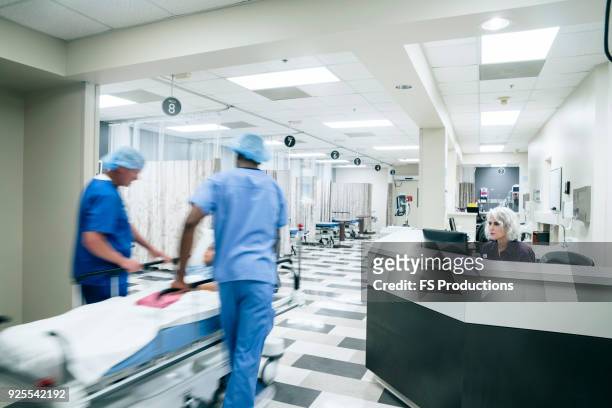 doctors pushing patient in hospital gurney - notaufnahme stock-fotos und bilder