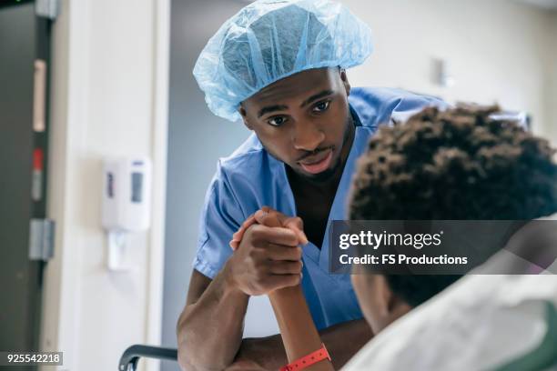 black doctor holding hand of boy in hospital bed - doctor african child stock-fotos und bilder