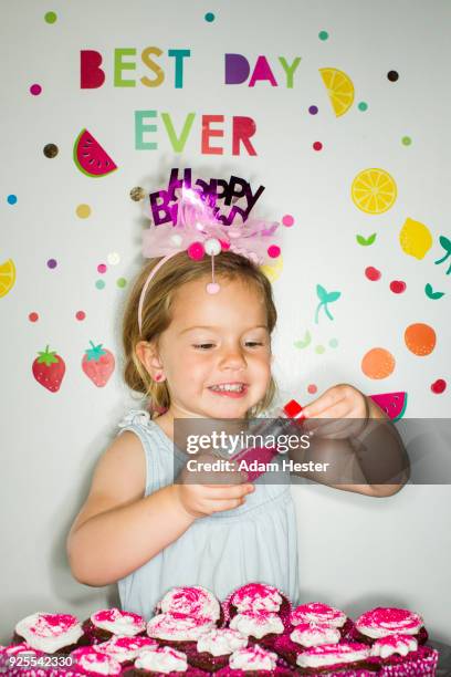 caucasian girl holding sprinkles over tray of cupcakes for birthday - hundreds and thousands stock pictures, royalty-free photos & images