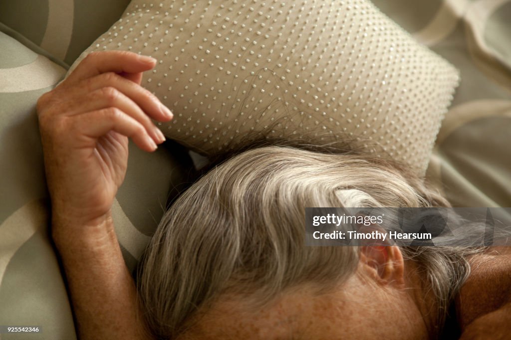 Close-up view of woman's hand and streaked gray hair against sequined pillow and comforter