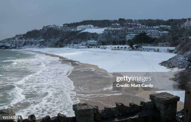 People walk on the snow covering the sand at Carbis Bay as snow arrives in St Ives on February 28, 2018 in Cornwall, England. Freezing weather...