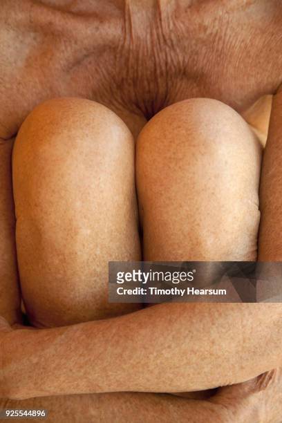 close-up view of an older woman's arms wrapped around her knees as she pulls them to her chest - timothy hearsum stockfoto's en -beelden