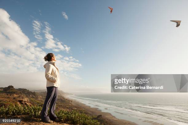 mixed race woman standing on beach watching gliders - deltaplane photos et images de collection