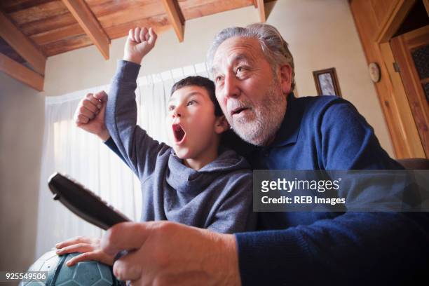hispanic grandfather and grandson cheering for soccer game on television - begeistert fernsehen stock-fotos und bilder
