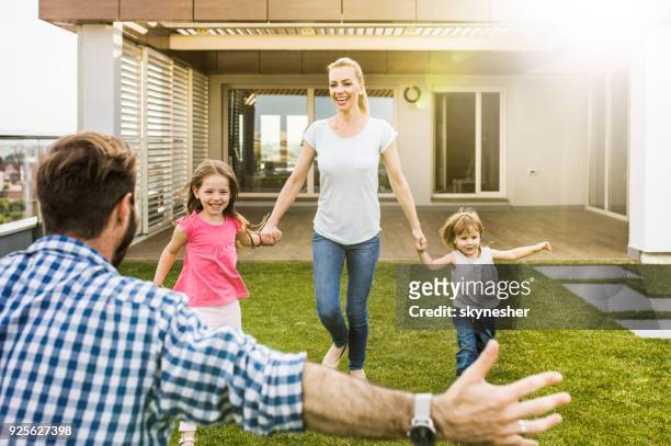 jugueton madre y los niños corriendo hacia el abrazo del padre en el balcón de un ático. - penthouse girl fotografías e imágenes de stock