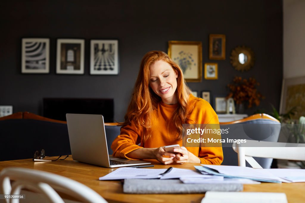 Smiling businesswoman using mobile phone at home