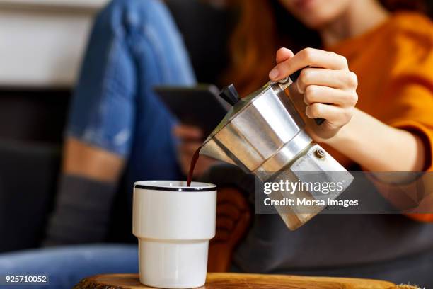 young woman pouring coffee into cup at home - transbordar imagens e fotografias de stock