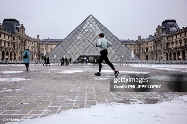 Man jogs past the Louvre Pyramid after overnight snowfall in Paris on March 1, 2018. Fresh heavy snowfalls and icy blizzards were expected to lash...
