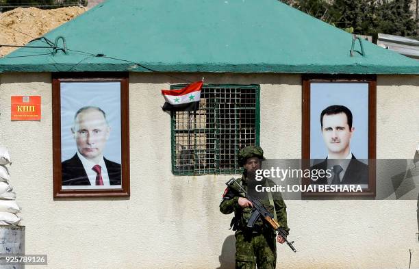 Picture taken on March 1, 2018 shows a member of the Russian military police standing guard between the portraits of Syrian President Bashar al-Assad...