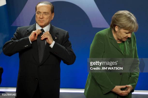 Italian Prime Minister Silvio Berlusconi adjusts his tie next to German Chancellor Angela Merkel before posing for a family photo on November 3, 2011...