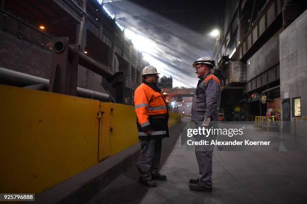 Employees talk in front of molten iron glows red hot inside a furnace at a mill of German steel producer Salzgitter AG on March 1, 2018 in...