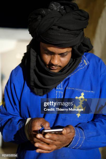 Man dressed as a Berber is looking at his smartphone in the fortified granary ruined Berber village of Douiret . Eddwirat or igherman was built on a...