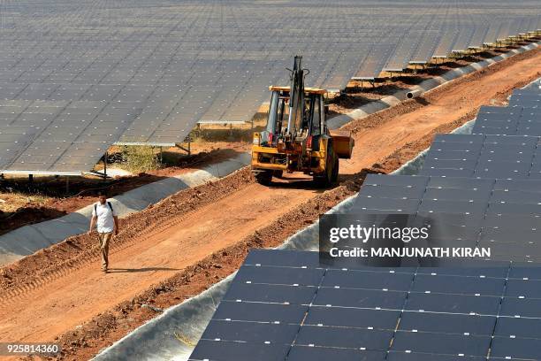 An earth mover passes amidst rows of solar panels at "Shakti Sthala", the 2000 Megawatt solar power park in Pavagada Taluk, situated about 150 kms...