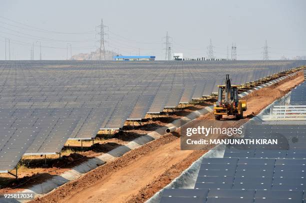 An earth mover passes amidst rows of solar panels at "Shakti Sthala", the 2000 Megawatt solar power park in Pavagada Taluk, situated about 150 kms...