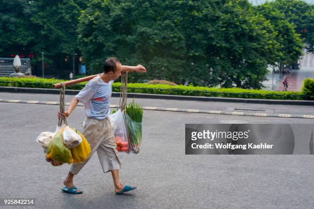 Man is carrying produce on a carrying pole, also called a shoulder pole, over the shoulders in Chongqing, China.