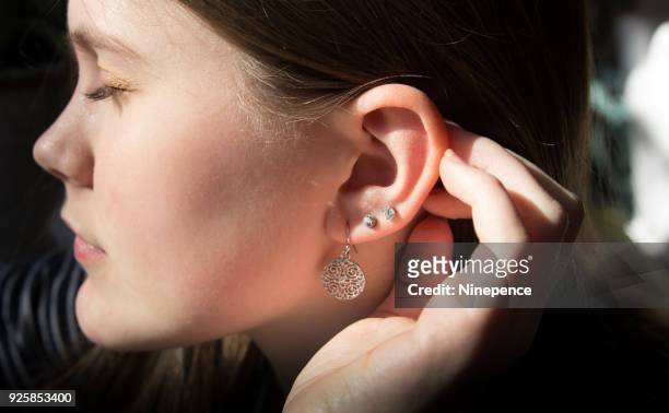 close up profile view of a teenage girl pushing her hair behind her hear - ear piercing stock-fotos und bilder