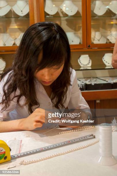Young woman is stringing pearl necklaces in the Fanghua Pearl and Jewelry store in Beijing, China.
