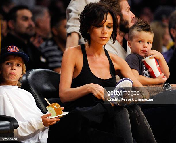 Victoria Beckham ties the shoe laces of her son Romeo as they follow the action on the floor with her husband David Beckham and their son Cruz...