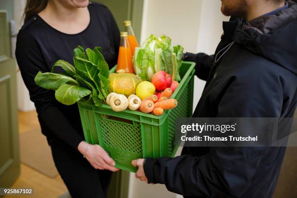 Berlin, Germany Posed Scene: A vegetable box scheme with fresh organic fruit and vegetables is handed over at the front door by a supplier to a...