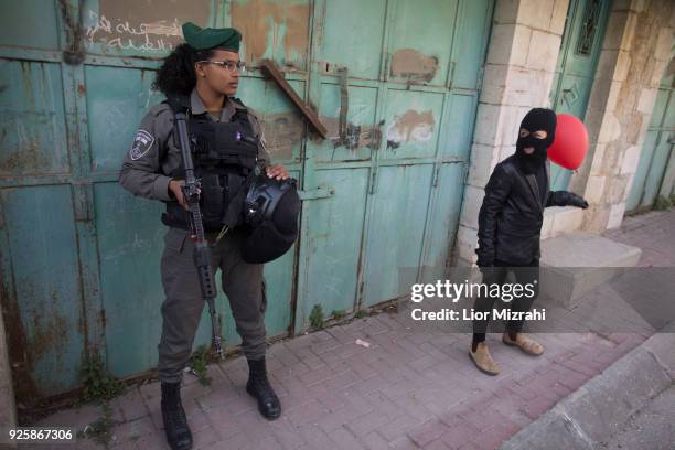 An Israeli woman soldier stand gaurds gaurd as Israelis take part in a parade celebrating the Jewish holiday of Purim on March 1, 2018 in Hebron,...