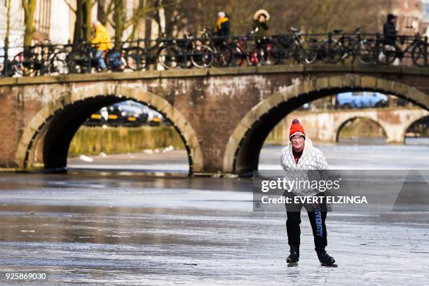 Skater skates on the ice of the lightly frozen Keizersgracht Canal in Amsterdam on March 1, 2018. - Heavy snowfall and deadly blizzards lashed...