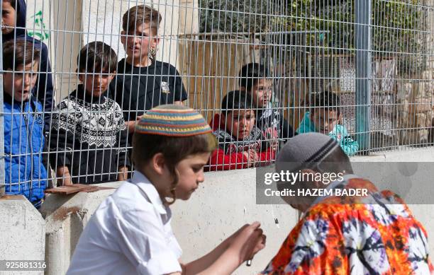 Palestinian youth watch as Israeli settlers celebrate the Jewish Purim holiday at al-Shuhada street in the divided West Bank town of Hebron, on March...