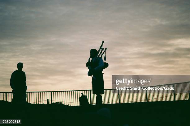 Bagpiper wearing traditional Scottish kilt is visible in silhouette against a sunset at the Ritz Carlton luxury hotel in Half Moon Bay, California,...