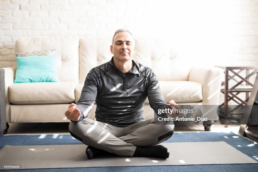 Mature man meditating in lotus pose at home