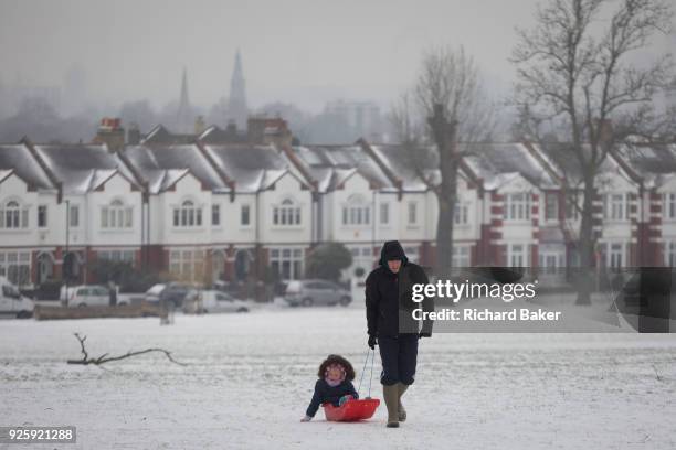 An adult pulls a child uphill on a small sledge in Ruskin Park, south London during the bad weather covering every part of the UK and known as the...