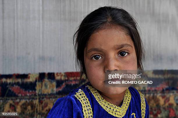 Five year old Afghan girl, Sahibah who learned to weave carpets before reading and writing, takes a break from helping other children weave a large...