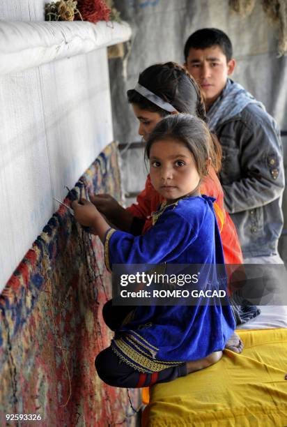 Five year old Afghan girl, Sahibah who learned to weave carpets before reading and writing, helps fifteen year old Enayat and nine year old Nafisah...