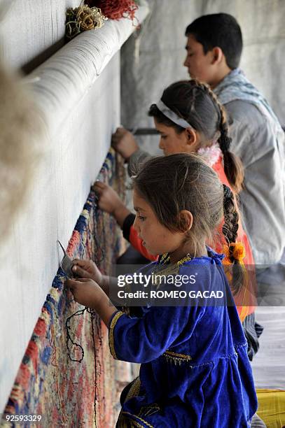 Five year old Afghan girl, Sahibah who learned to weave carpets before reading and writing, helps fifteen year old Enayat and nine year old Nafisah...