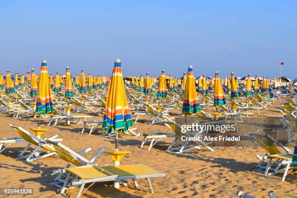beach with folded umbrellas and sun chairs, bibione, veneto, italy - bibione stock pictures, royalty-free photos & images