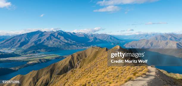 view of mountains and lake, woman jumping at top ridge, roys peak, lake wanaka, southern alps, otago region, southland, new zealand - region otago stock pictures, royalty-free photos & images