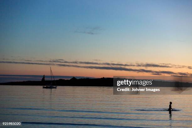 silhouette of person bathing in water against sailboat at sunset - kinder badeboot stock-fotos und bilder