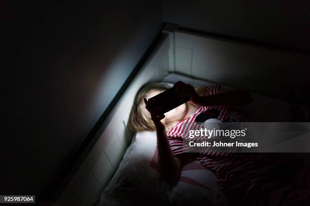 girl using smartphone in dark room while lying in bed - children in need stock-fotos und bilder