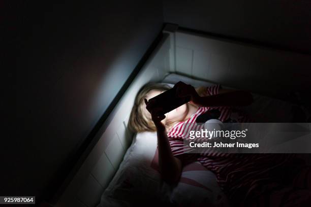 girl using smartphone in dark room while lying in bed - weakness stock pictures, royalty-free photos & images