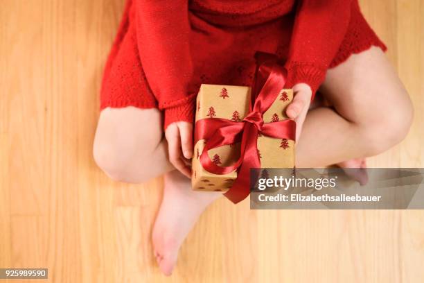 overhead view of a girl sitting cross-legged holding a wrapped christmas gift - bow legged stock pictures, royalty-free photos & images