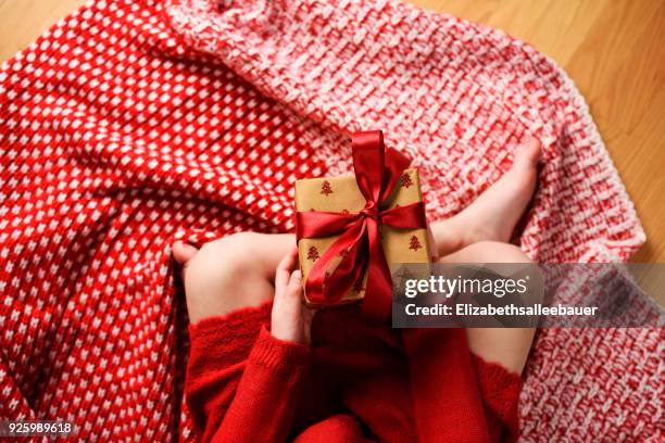 overhead view of a girl sitting cross-legged holding a wrapped christmas gift - bow legged stock pictures, royalty-free photos & images